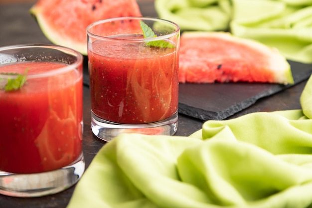 Watermelon juice with chia seeds and mint in glass on a black concrete background with green textile. Healthy drink concept. Side view,  close up, selective focus.