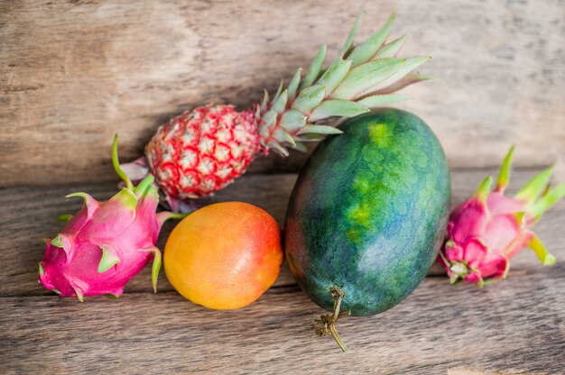 Watermelon near mango pineapple and dragon fruit on the old wooden background