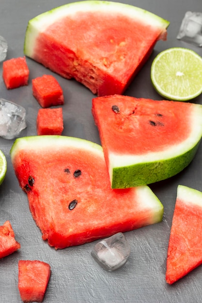 Watermelon slices lime half and ice on gray