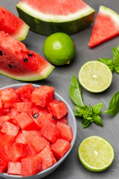 Watermelon slices lime halves and sprig of basil on table Sliced watermelon pulp in bowl