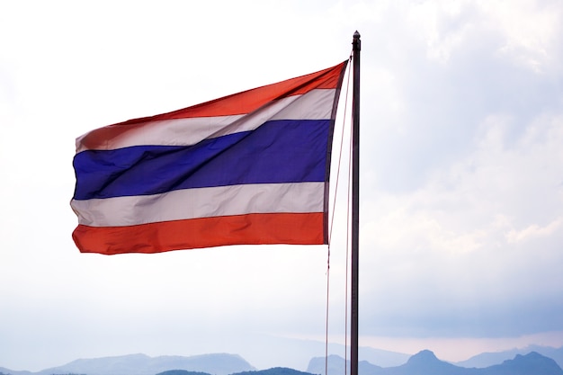 Waving Thai flag of Thailand with blue sky and mountain background