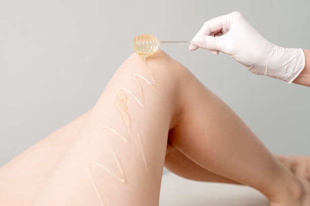 Wax ax flows down the honey stick on leg during hand holding stick concept of depilation and epilation