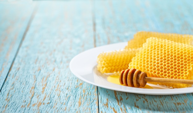 Wax honeycombs from a bee hive filled with natural  honey in white plate on  blue rustic table,  with copy space for text.