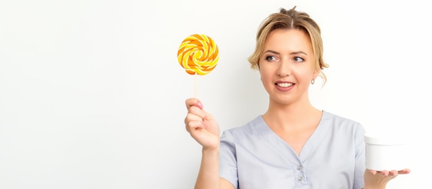 Waxing depilation concept The beautician is wearing a medical coat holding a sugar lollipop with a jar of sugar paste on white background