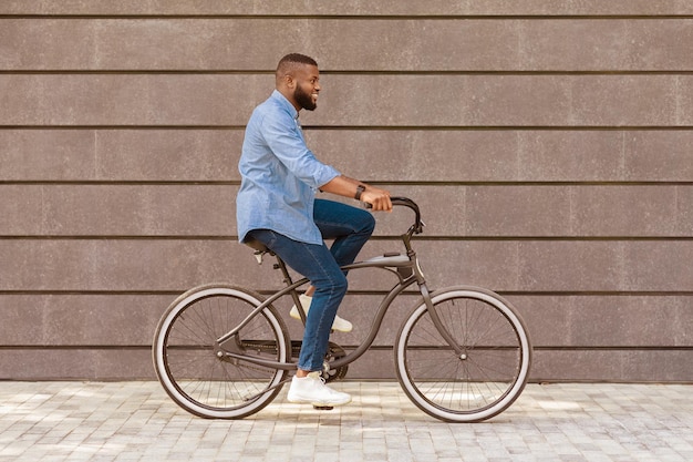 Photo way to office young african american businessman riding bicycle against urban wall background going