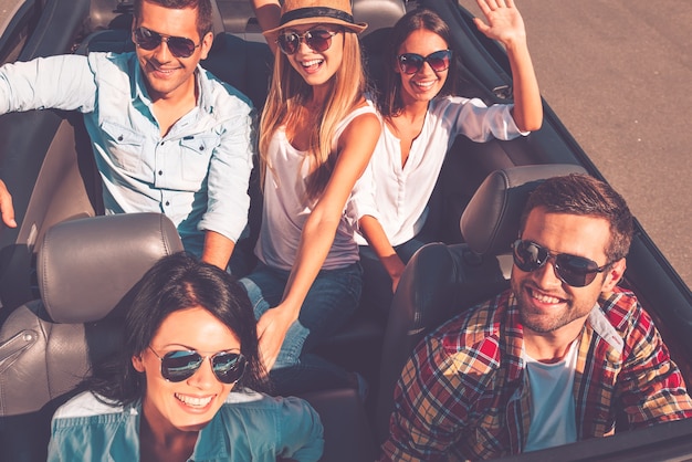 We always travel together. Top view of young happy people enjoying road trip in their white convertible and raising their arms