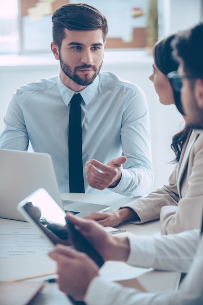 We have new business plan! Close-up part of young handsome man gesturing and discussing something with his coworkers while sitting at the office table