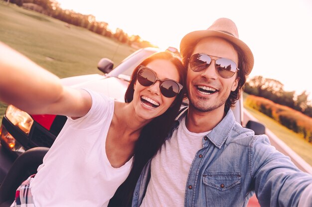 We love selfie! Beautiful young couple bonding to each other and leaning at their pick-up truck while making selfie