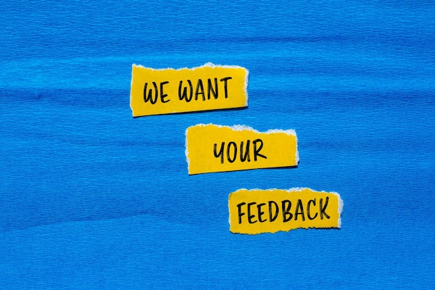 Photo we want your feedback message written on ripped torn yellow paper pieces with blue background conceptual we want your feedback symbol copy space