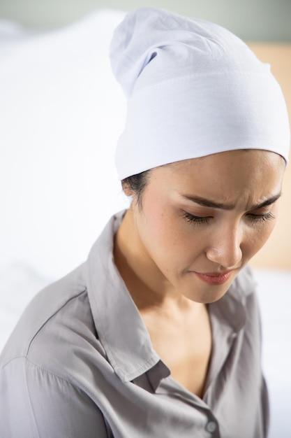 Weak asian woman cancer patient wearing head scarf after suffering serious hair loss and pain due to chemotherapy