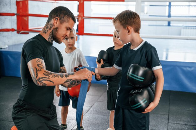 Photo wearing blue hand wraps young tattooed coach teaching the kids boxing techniques