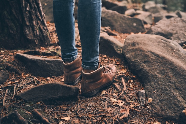 Wearing comfortable boots. Close-up of modern woman standing in the forest while enjoying her travel in mountains