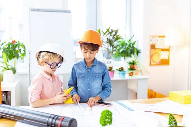 Wearing crash helmets. Cute schoolboys wearing crash helmets feeling curious painting sketches