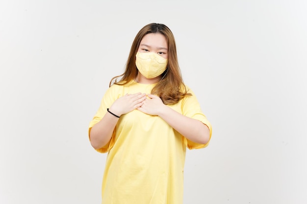 Wearing Mask and Hands on Chest of Beautiful Asian Woman wearing yellow TShirt Isolated On White