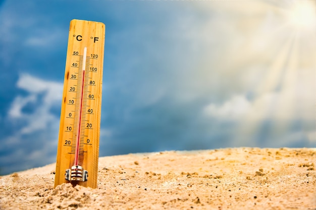 Weather thermometer in the sand against the sky showing a high ambient temperature