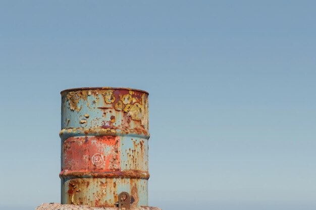 A weathered oil drum stands tall showcasing vibrant colors and a distinct logo under a bright blue sky evoking a sense of isolation and resilience in nature