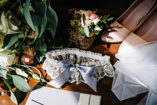 Photo wedding accessory bride stylish beige shoes bouquet of flowers garter on table standing on wooden background silhouette and shadow sunshine letters from the bride and groom