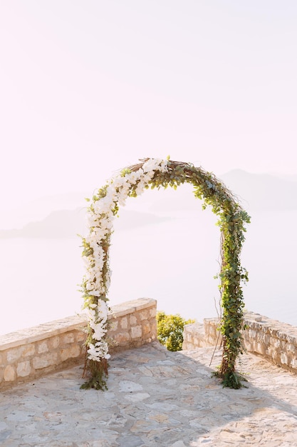 Photo wedding arch decorated with white orchids stands on the observation deck above the sea