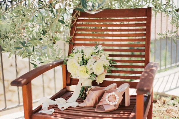 Wedding bouquet stands on a wooden armchair next to the bride sandals