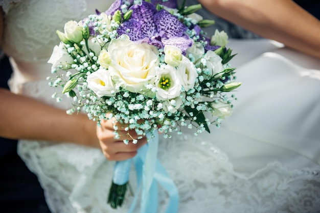 Wedding bouquet of white and lilac flowers in hands of a young bride, close-up. Horizontal image, selective focus. Happy marriage day concept.