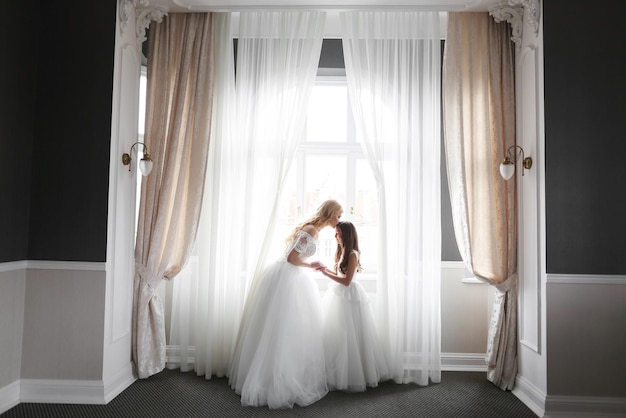 Wedding Bride in beautiful dress sitting on sofa indoors in white studio interior like at home Trendy wedding style shot in full length Young attractive caucasian brunette model like a bride