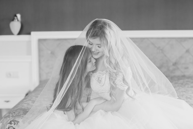 Wedding Bride in beautiful dress sitting on sofa indoors in white studio interior like at home Trendy wedding style shot in full length Young attractive caucasian brunette model like a bride