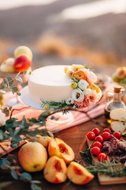 Wedding cake decorated with flowers stands on a table among fruits and vegetables