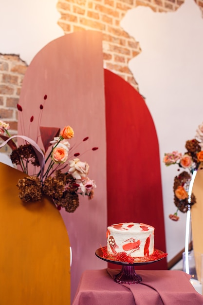 Wedding cake near wedding arch with flowers in interior with brick walls.