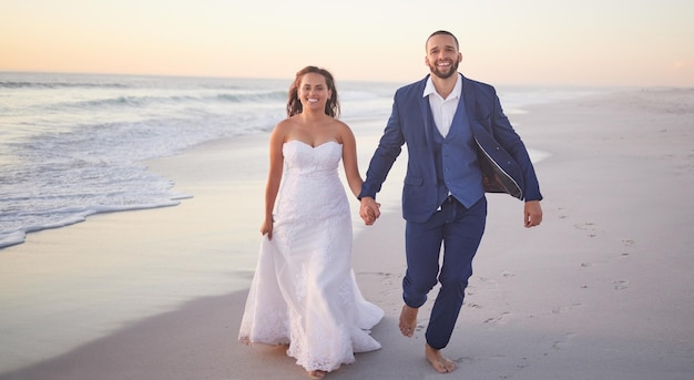 Wedding couple and beach with a man and woman holding hands while walking on the sand by the ocean or sea Love trust and marriage with a bride and groom on the coast at sunset for celebration