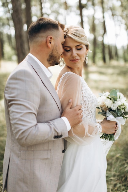 Wedding couple bride and groom hugging in pine forest sunlight filtering through the trees highlighting their joyful expressions