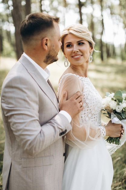 Wedding couple bride and groom walk hand in hand through a pine forest sunlight filtering through the trees highlighting their joyful expressions