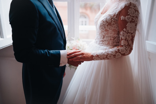 Wedding couple dressed in wedding suits delicately holding hands. The wedding ring is appreciated.