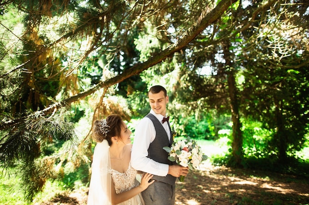 A wedding couple enjoys walking in the woods. Newlyweds hug and hold hands