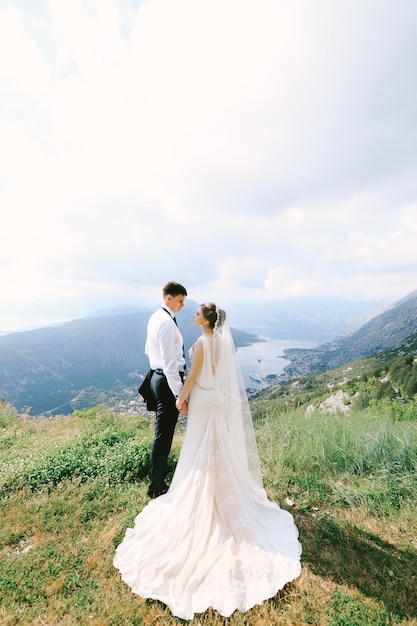 Wedding couple hold hands on the top of mount lovcen against the backdrop of the kotor bay