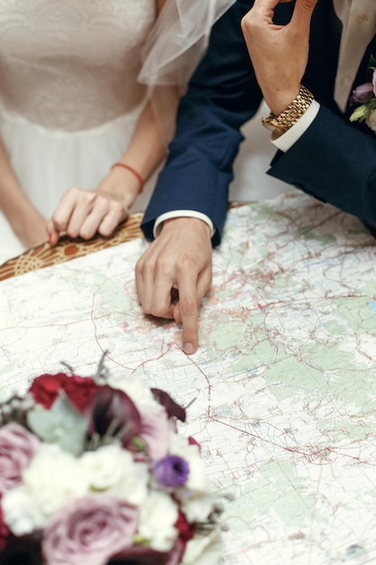 Wedding couple planning honeymoon stylish bride and groom looking at map talking about summer travel vacation sitting at wooden vintage table in cafe