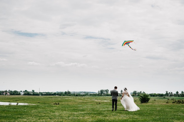 A wedding couple running back around field letting kite fly and hold the kite Bride and groom walk.