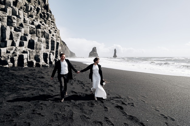 Wedding couple walks along the black beach Vik in Iceland