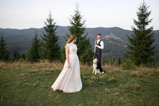 Wedding couple with dog in mountains at sunset romantic evening in mountains