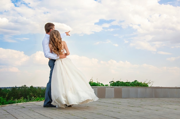 Wedding Day. Beautiful Bride in the Arms of the Groom on Sky