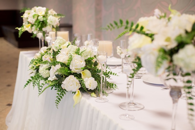 Wedding decor in the interior, White flowers on the table, Serving the table with crystal glasses.