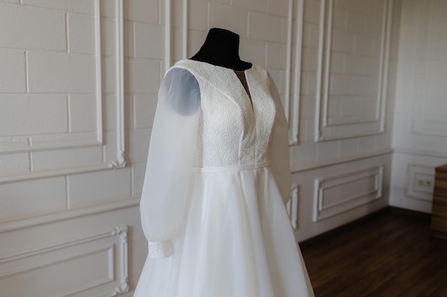 A wedding dress on a mannequin in a room with a wall behind it.