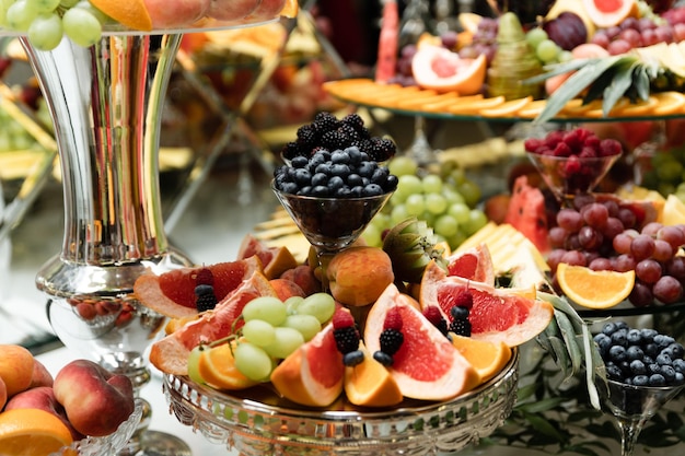 Photo wedding fruit table on which various exotic fruits and sweets. candy bar with fruits. pears, apples, pineapples and many other food at the banquet