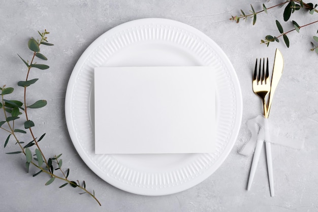 Wedding invitation card mockup 7x5 on white plate on grey background with eucalyptus Menu card festive table setting