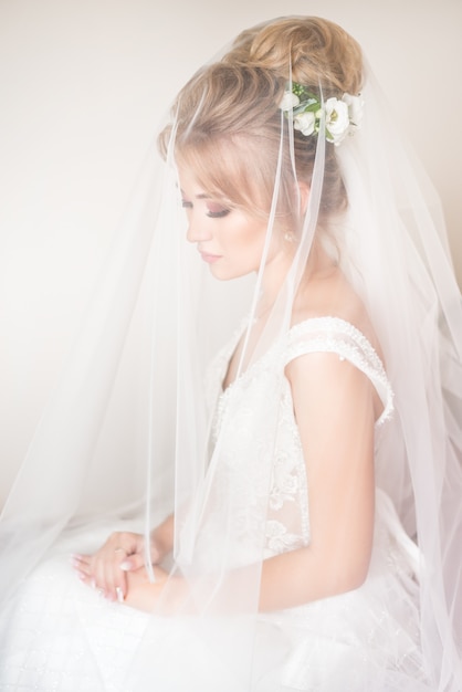 The wedding morning. Beautiful portrait of the bride covered with a veil. Eyes look down. hairstyle with fresh flowers.