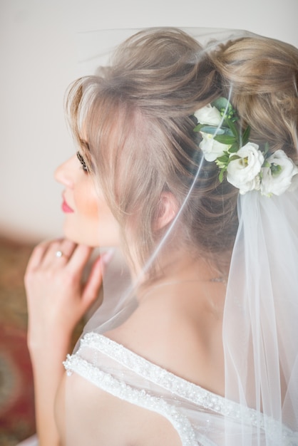 The wedding morning. Beautiful portrait of the bride covered with a veil. Eyes look down. hairstyle with fresh flowers.