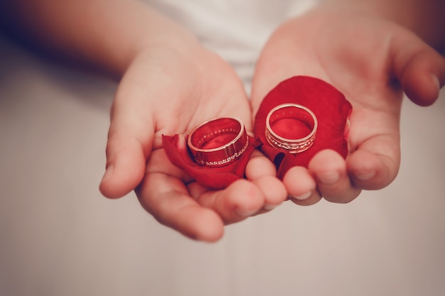 Photo wedding rings lie on children's palms with petals of roses