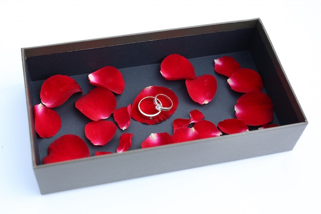 Wedding rings on petals of red rose in luxury leather box