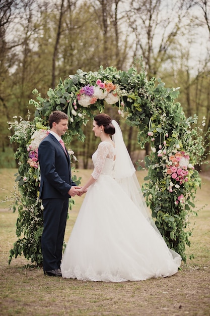 Wedding in the spring. Ceremony on the street. An arch of real flowers. The bride and groom look at each other.