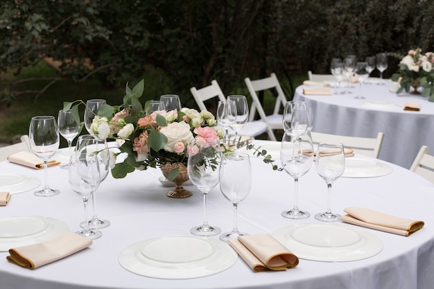 Wedding table setting decorated with fresh flowers in a brass vase. Banquet table for guests outdoors with a view of green nature