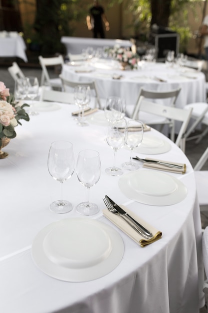 Wedding table setting decorated with fresh flowers in a brass vase. Wedding floristry. Banquet table for guests outdoors with a view of green nature. Bouquet with roses, eustoma and eucalyptus leaves